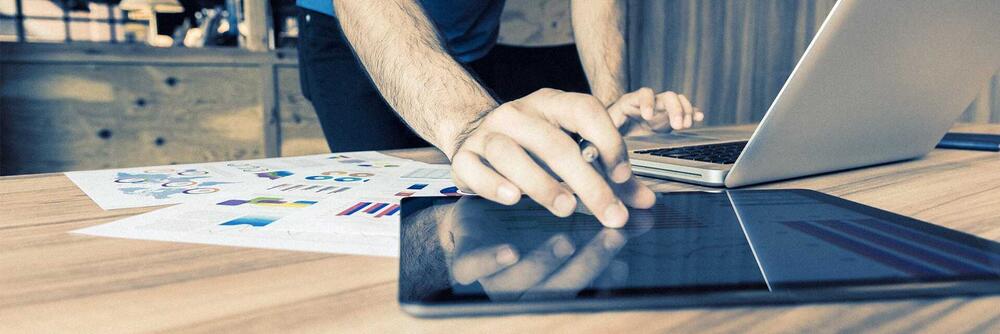 Ein Mann verwendet an einem Schreibtisch zeitgleich ein Notebook und ein Tablet.