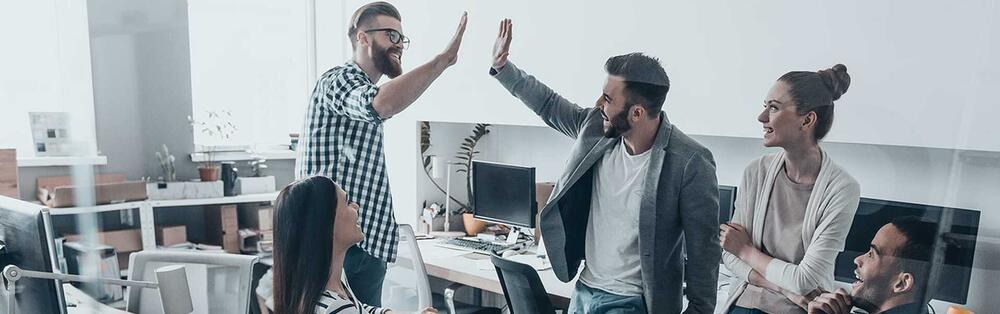 Eine Gruppe Personen unterhält sich ein einem Büro. Zwei Männer schlagen mit ihren Händen ein.