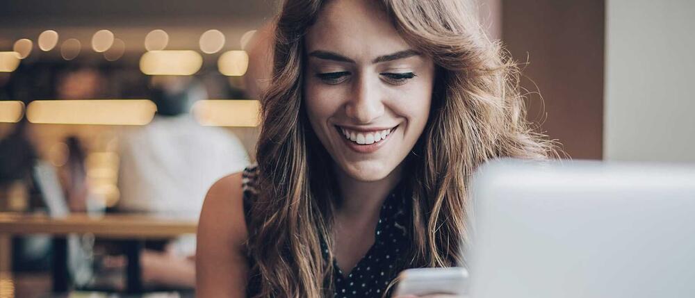 Eine Frau sitzt in einem Café und nutzt ihr Smartphone.