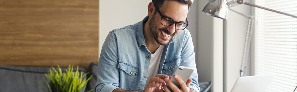 Ein Mann sitzt an einem Schreibtisch und bedient sein Smartphone.